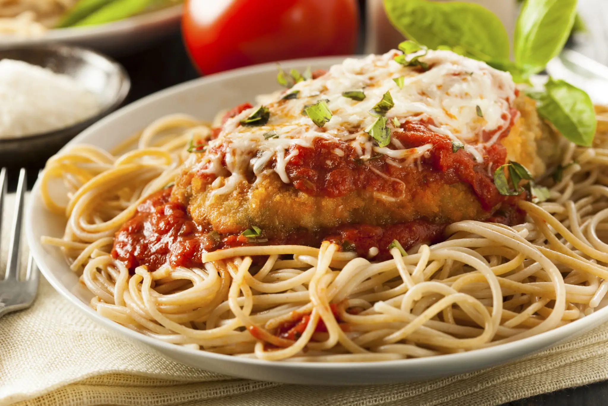 Plate of spaghetti topped with chicken parmesan and marinara sauce.