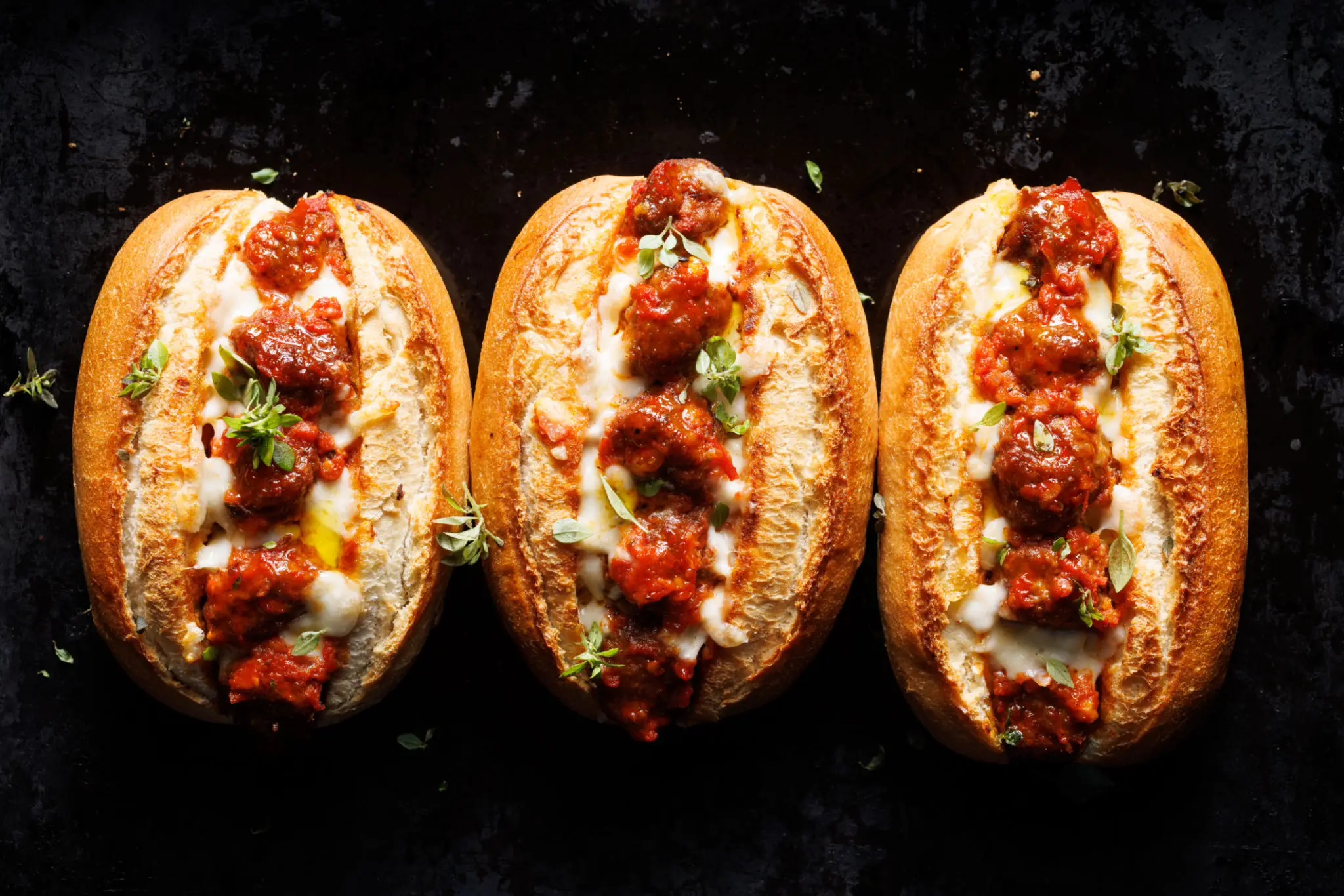 Three meatball subs with melted cheese and marinara sauce.