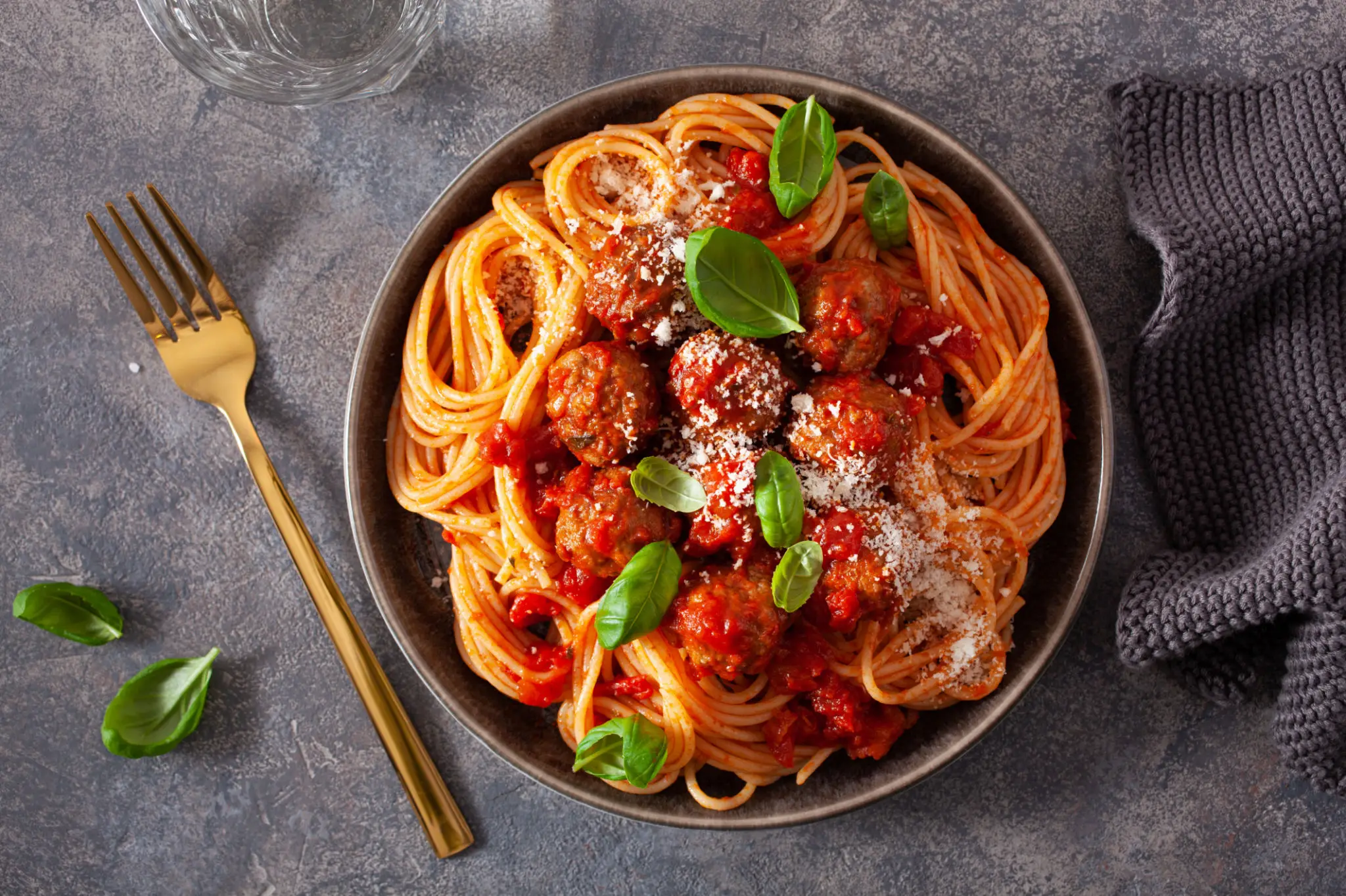 A bowl of spaghetti with tomato sauce, garnished with basil and grated cheese.