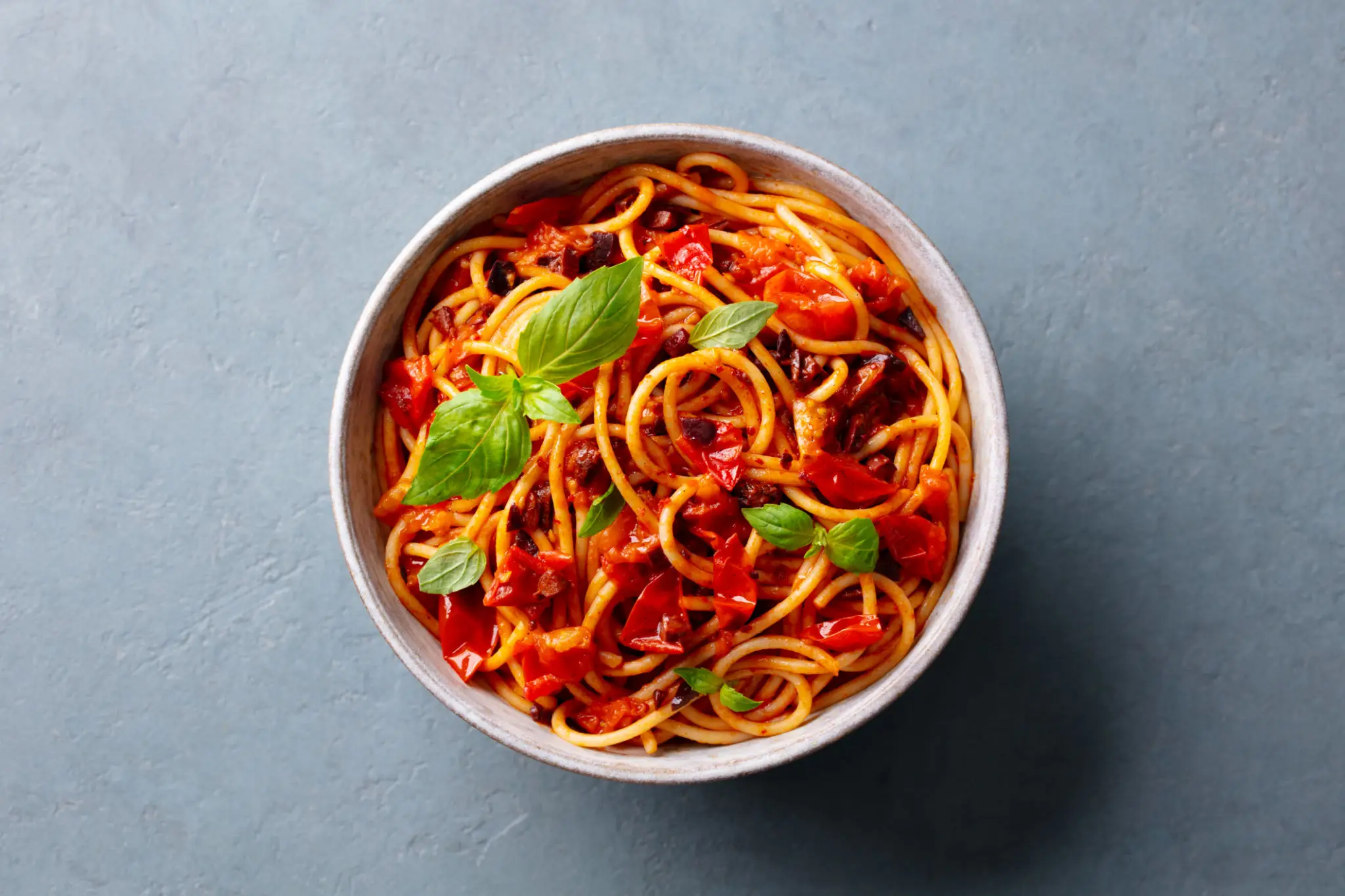 A bowl of spaghetti with tomato sauce and fresh basil leaves.